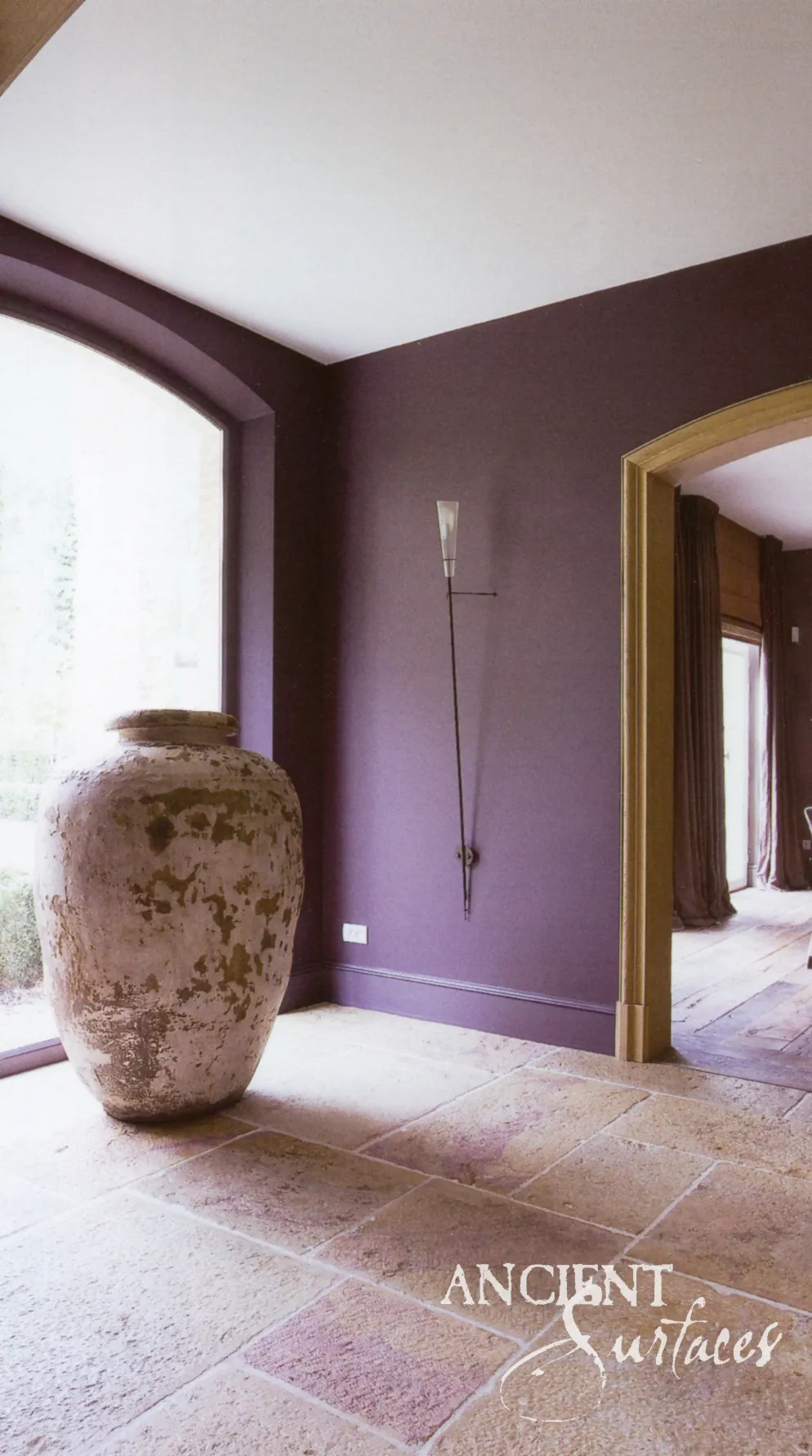 Antique stone urn on a reclaimed limestone flagstone floor against a deep plum wall